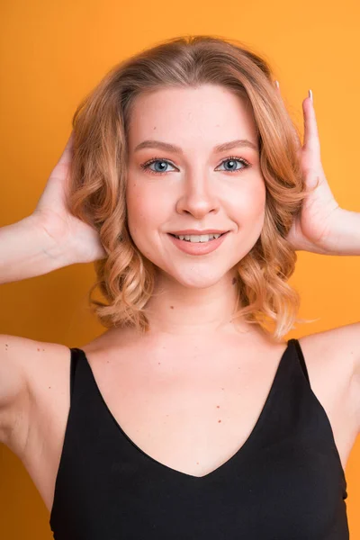 Um retrato de uma menina europeia bonito consertar o cabelo e sorrindo, isolado no fundo laranja. Radiante, brilhante maquiagem natural — Fotografia de Stock
