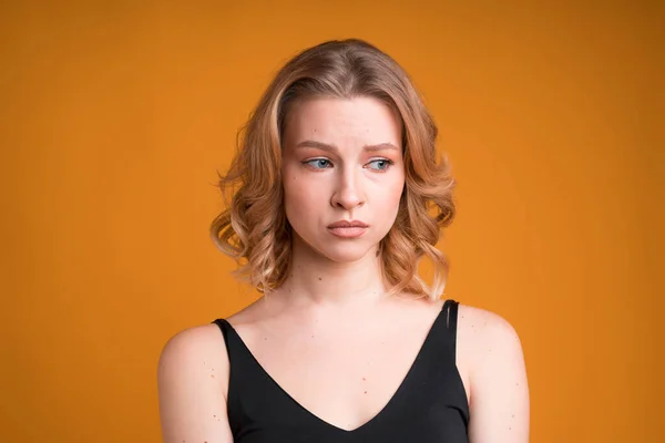Ένα πορτραίτο μιας κυκλοθυμικής καυκάσιας κοπέλας, απομονωμένης σε πορτοκαλί φόντο. Είναι απογοητευμένη και λυπημένη, κοιτάει στο πλάι και μουτρώνει τα χείλη. — Φωτογραφία Αρχείου