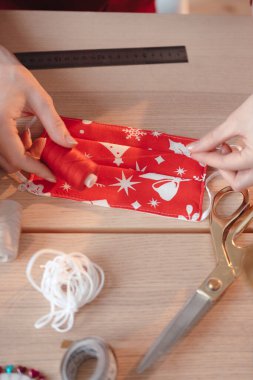 Koronavirüsten korumak için yeni yıl ya da Noel baskılı DIY tıbbi maskesinin en üst görüntüsü. Dikiş aletleri, terzi makası, iplikler, iğne çubuğu.