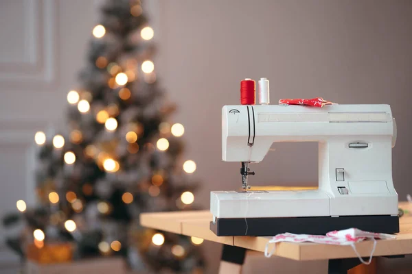 Üzerinde iki kırmızı ve beyaz iplik ve arka planda bir Noel ağacı olan bir dikiş makinesinin ticari çekimi. — Stok fotoğraf