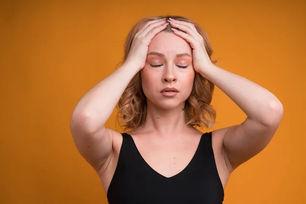 オレンジ色の背景に隔離された穏やかなしようとしている頭痛の種の若い女性の肖像画 — ストック写真