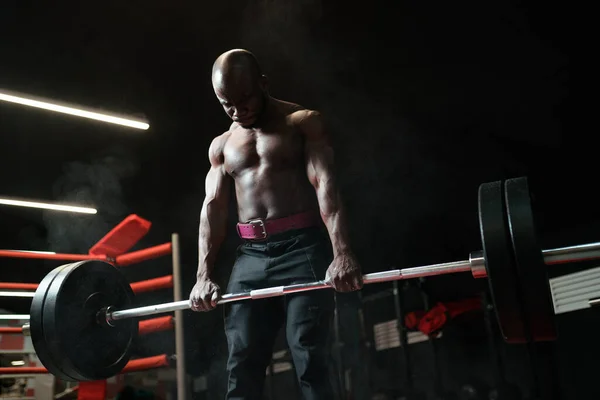 Muscular african american man weightlifter or bodybuilder doing exercises with a barbell in the gym — Stock Photo, Image