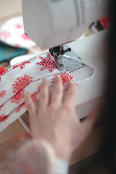 As mãos de uma mulher costuram em uma máquina de costura uma máscara médica de Ano Novo durante a pandemia do coronavírus. Faça-você-mesmo máscara protetora brilhante festiva contra vírus — Fotografia de Stock