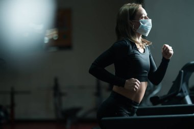 Sağlık maskeli bir fitness eğitmeni koşu bandında, koronavirüs salgını sırasında akciğerlerini geliştiriyor.
