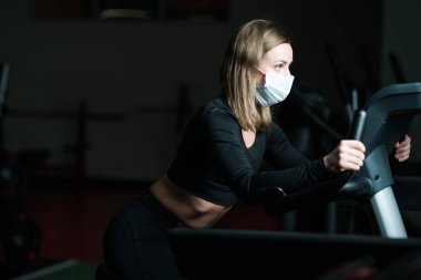 Sağlık maskeli bir fitness eğitmeni koşu bandında, koronavirüs salgını sırasında akciğerlerini geliştiriyor..