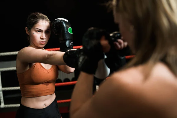 Two Caucasian female boxers are fighting in the ring. Boxing training in the gym