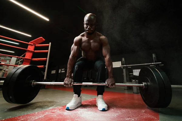 Homem Africano americano muscular levanta uma barra pesada para powerlifting. Peso pesado na fumaça de talco em pó ou magnésia — Fotografia de Stock