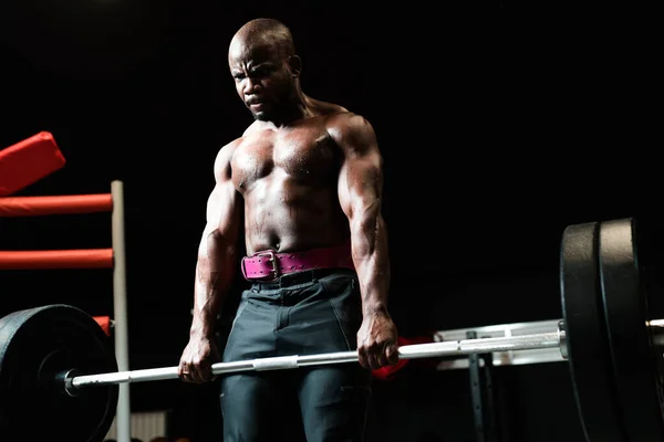 Vista inferior. Um homem musculoso com um tronco nu, um powerlifting ou musculação treinador fica com uma barra em suas mãos. — Fotografia de Stock