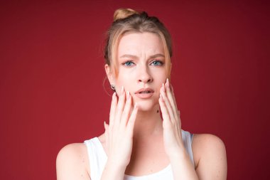 Beyaz tişörtlü sarışın kadın kırmızı arka planda izole edilmiş diş ağrısından muzdarip..