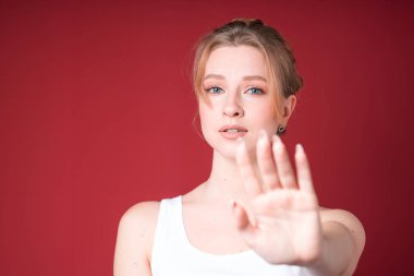 Beyaz kolsuz bluzlu korkunç sarışın kadın kırmızı arka planda Covid-19 'dan dolayı mesafeyi korumanı söylüyor..