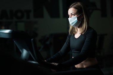 Küresel covid-19 virüsü salgınında kendini koronavirüsten korumak için koşu bandında antrenman yapan ve maske takan Kafkas sporcu kadın.