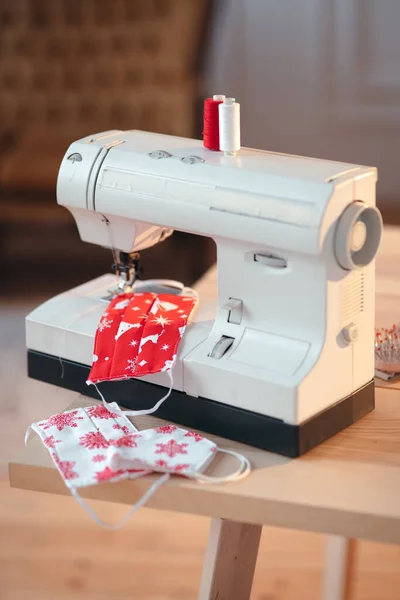 Werbeaufnahme einer Nähmaschine mit weihnachtlich gemusterten DIY-Gesichtsmasken und zwei Fäden. Heimbüro der Näherin — Stockfoto