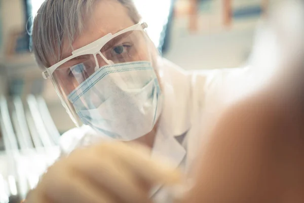 Zbliżenie twarzy męskiego lekarza dentysty w masce ochronnej i goglach w procesie pracy z pacjentem. Dentysta leczy zęby. — Zdjęcie stockowe