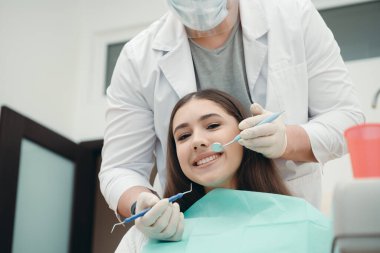 Doktor çenesini diş cımbızıyla incelerken güzel kız gülümsüyor. sağlıklı diş konsepti