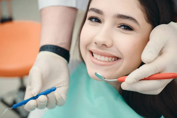Gelukkige brunette kijkend naar de camera naast welke medische hulpmiddelen. Portret van een meisje bij een tandarts afspraak — Stockfoto
