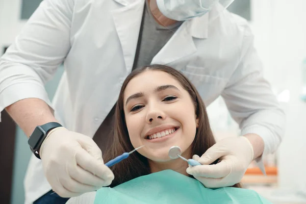 Vrouw glimlacht breed naar de camera terwijl de dokter haar tanden onderzoekt. Portret van een meisje bij een tandarts afspraak — Stockfoto