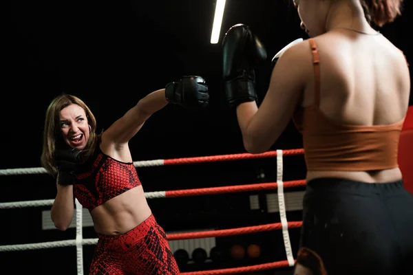 Сильная спортсменка в красной спортивной форме и черные мощные боксерские перчатки во время боя. Концепция бокса — стоковое фото