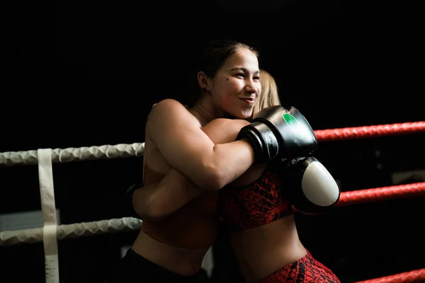 Duas raparigas de uniforme desportivo abraçam-se depois de uma luta no ringue. Boxe feminino, lutas sem regras — Fotografia de Stock