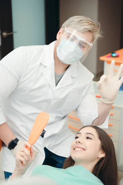 Tandarts met een beschermend masker en handschoenen en een klant die het resultaat controleert — Stockfoto