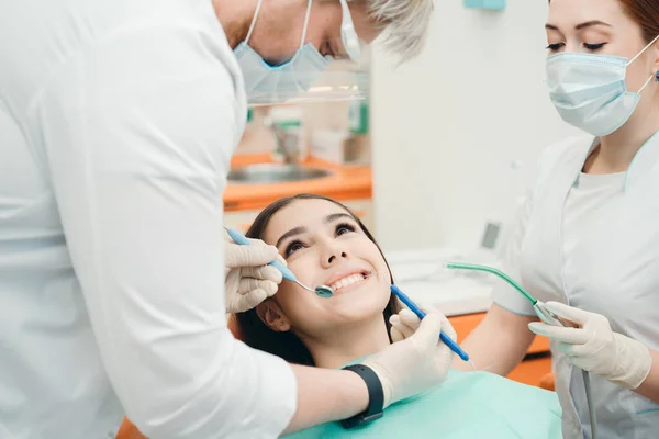 Glimlachen brunette liggend in de tandartspraktijk terwijl artsen de procedure uit te voeren — Stockfoto