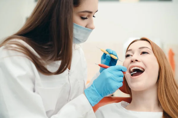 Een gemaskerde brunette onderzoekt de tanden van een klant met behulp van speciale medische hulpmiddelen — Stockfoto