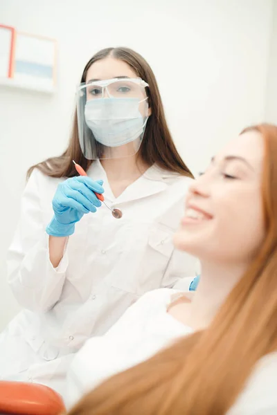 Een vrouw met een mooie glimlach ligt in een stoel terwijl de tandarts zich voorbereidt op de procedure — Stockfoto
