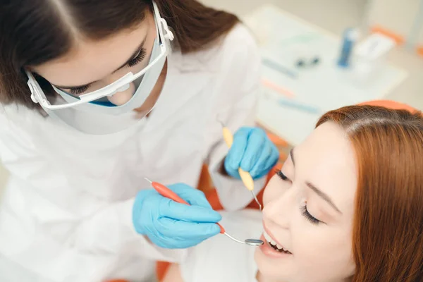 De tandarts maakt tanden reinigen om een mooie roodharige meisje met de hulp van speciale gereedschappen — Stockfoto