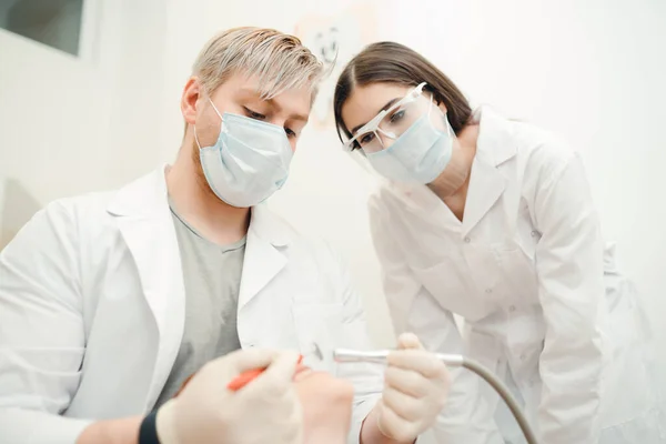 Specialisten in witte jassen verwijderen cariës van een patiënt in een kliniek. Gezonde tanden — Stockfoto