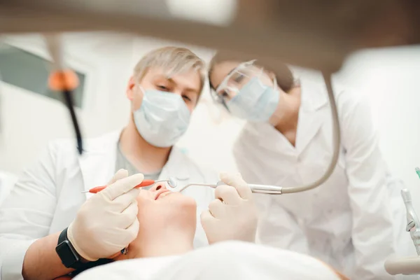 Twee tandartsen met medische maskers bleken tegen een meisje op de bank. — Stockfoto