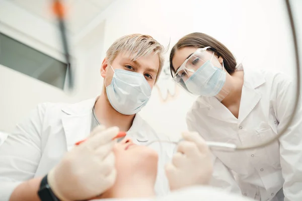 De arts voert de tandheelkundige behandeling procedure voor de klant, terwijl de assistent kijkt naar het — Stockfoto