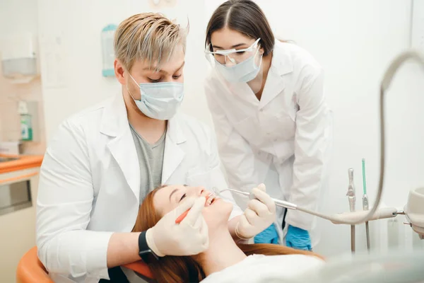 Twee tandartsen in witte jassen voeren tanden bleken procedure voor een roodharig meisje — Stockfoto