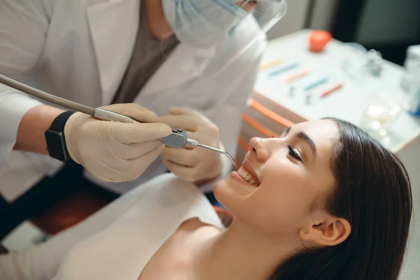 Dokter in medische handschoenen verwijdert cariës van een brunette liggend in een stoel — Stockfoto