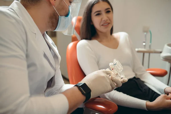 De brunette zit op de bank en de tandarts toont haar een model van tanden — Stockfoto