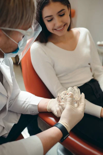 Een arts in medische handschoenen vertelt een meisje hoe om te gaan met haar tanden met behulp van een kaak model — Stockfoto