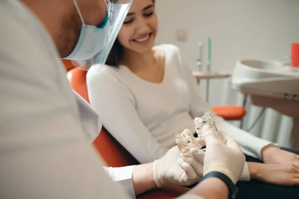 Tandarts in een beschermend masker toont een blank meisje een model van de kaak — Stockfoto