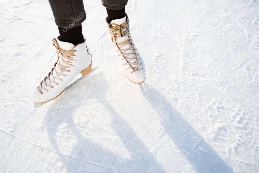 Photo of female legs in white skates that skate on ice. Winter weekend concept