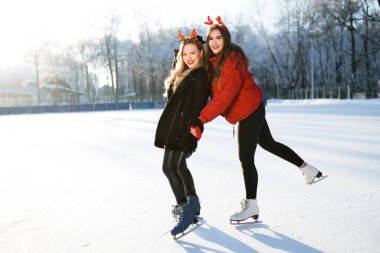 İki güzel kız. Biri diğerini tutuyor. Parkta buz pateni yaparken eğleniyorlar.