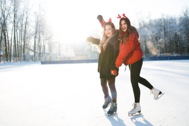 Dalgalı saçlı güzel beyaz kadınlar buzda kayıyorlar. Karlı güneşli bir gün