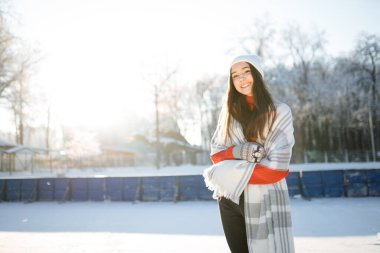 Beyaz şapkalı beyaz kız karlı bir parkta donmuş bir nehirde paten kayıyor.