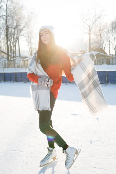 Uma menina com cabelos longos fica em patins em um chapéu e mitenes em um dia gelado ensolarado — Fotografia de Stock