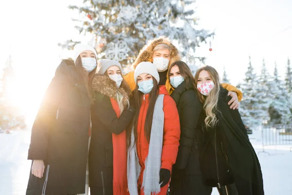 Grupo de amigos em roupas quentes usando máscaras médicas abraçando em uma floresta nevada — Fotografia de Stock