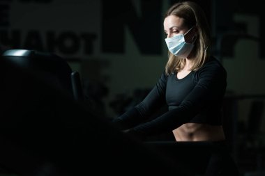 Sağlık maskeli bir fitness eğitmeni koşu bandında, koronavirüs salgını sırasında akciğerlerini geliştiriyor.
