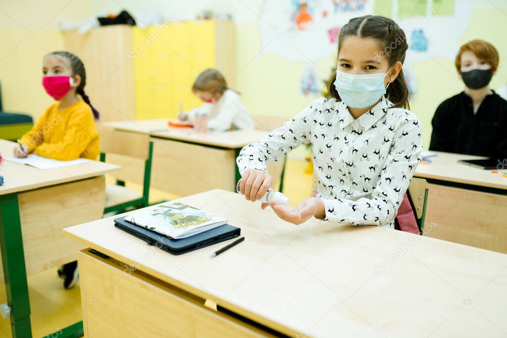 A girl in a white shirt in a medical mask is in the lesson and uses a hand sanitizer
