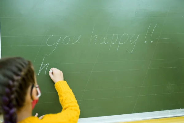 En vacker flicka i skyddsmask skriver på skolstyrelsen. Lektioner under coronavirus — Stockfoto