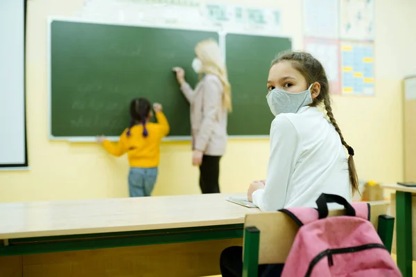 Un estudiante se sienta en un escritorio de la escuela mientras un maestro le explica una lección a un niño en el fondo —  Fotos de Stock