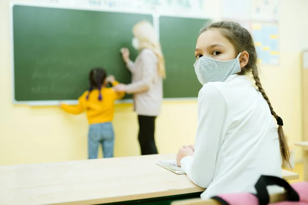 한 학생이 학교 책상에 앉아 있고, 한 교사가 뒤에 있는 어린이에게 한 가지 교훈을 설명 해 주고 있다 — 스톡 사진