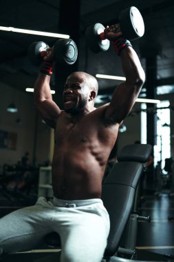 Gri pantolonlu çıplak bir adam trapezius kaslarını güçlendirmek için egzersiz yapar.