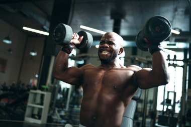 Gri pantolonlu çıplak bir adam trapezius kaslarını güçlendirmek için egzersiz yapar.