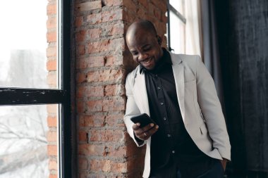 İş kıyafeti giymiş çekici bir Afro-Amerikalı çatı katında elinde telefonla dikiliyor. İş adamı sorunları çevrimiçi çözüyor