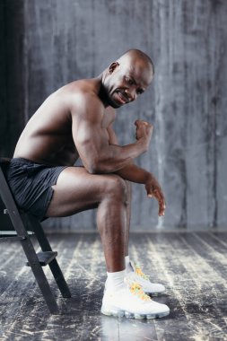 Kaslı, koyu tenli bir adam oturur ve pazılarını sertçe gösterir. Sağlıklı yaşam tarzı kavramı